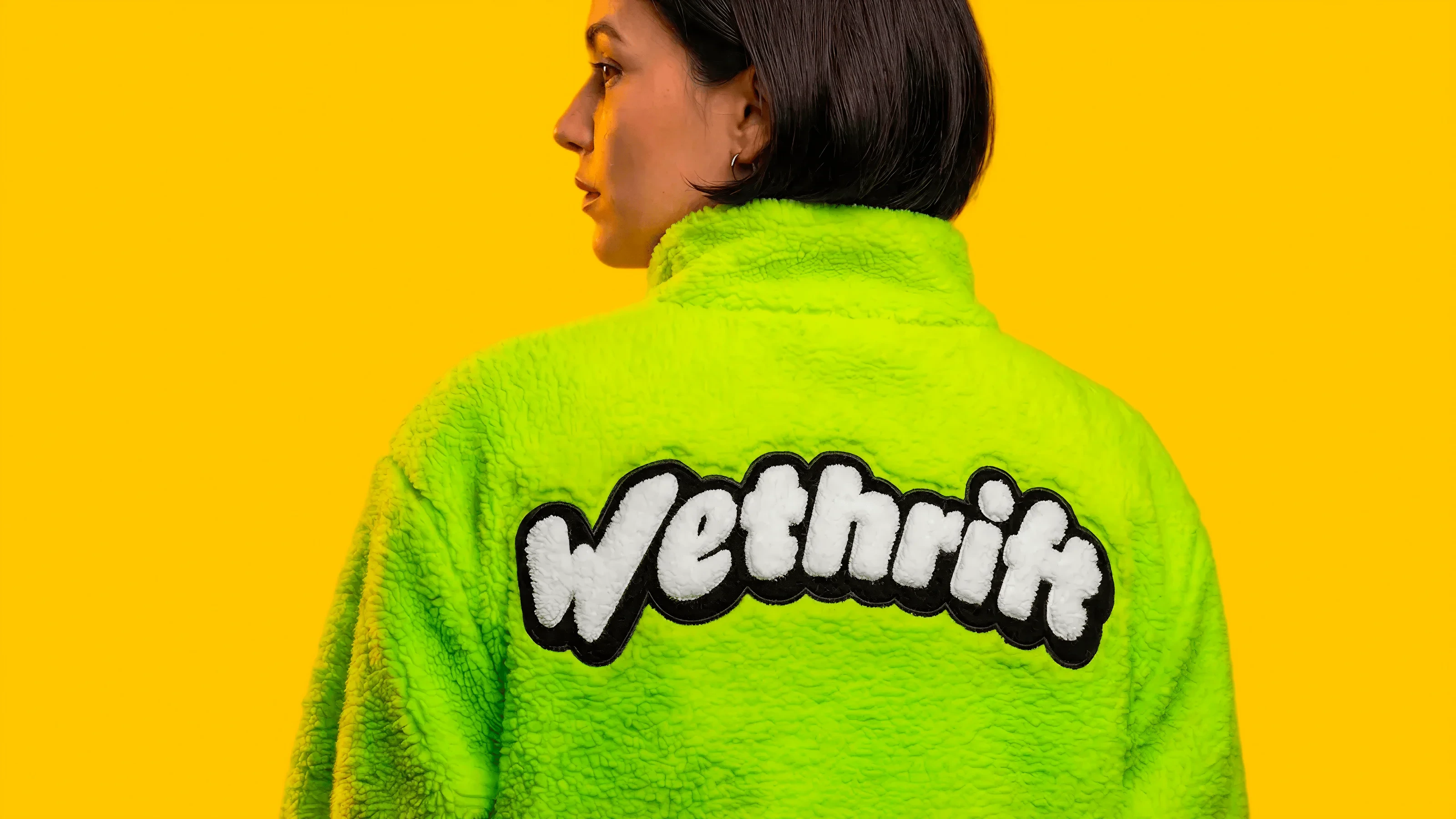 Person wearing a lime green fleece with a Wethrift chenille patch on the back